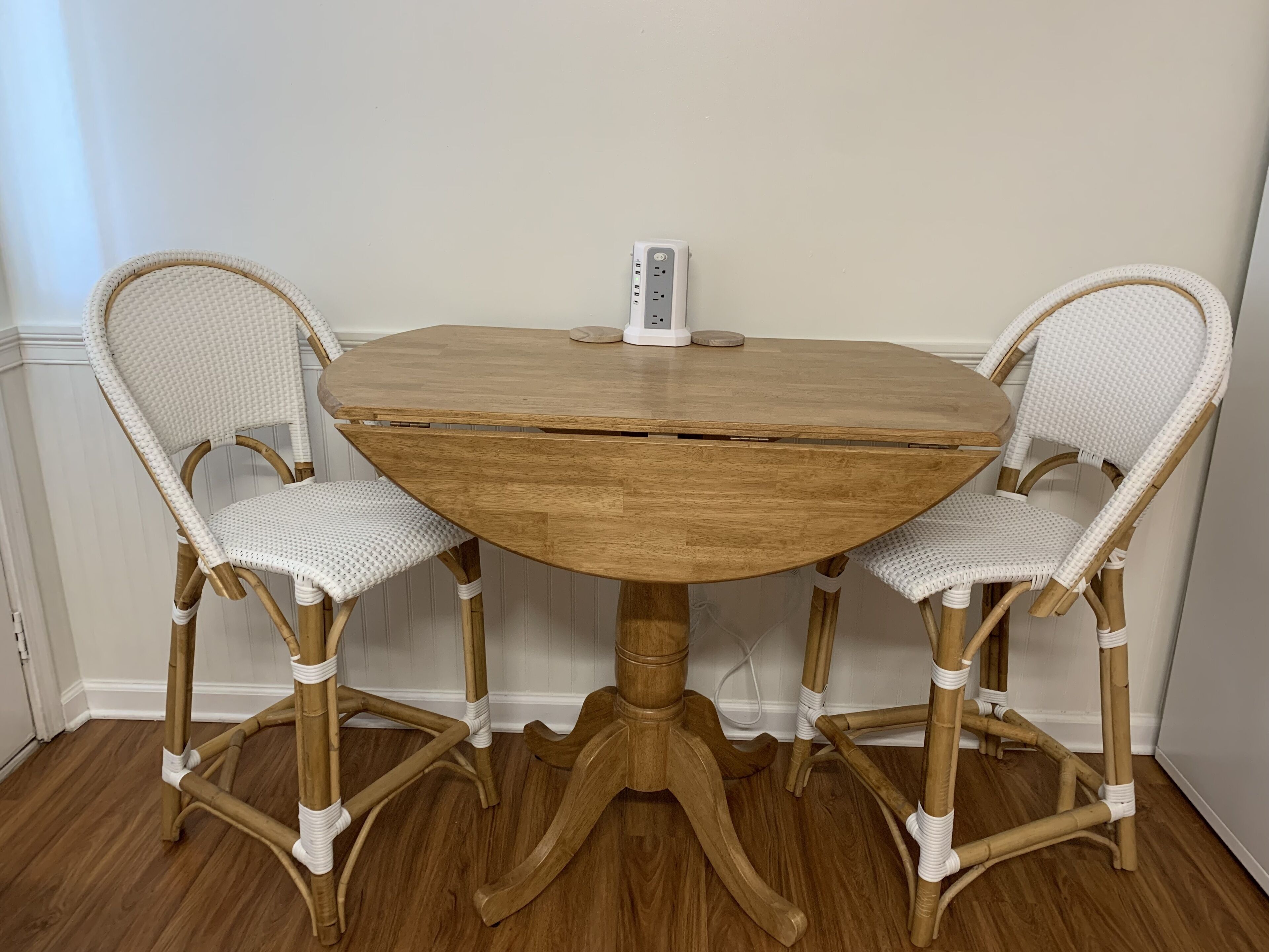 Uma mesa de madeira redonda com duas cadeiras de vime branco.