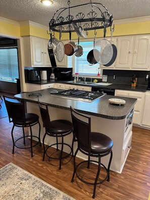 A kitchen with a central island, bar stools, and hanging pots. - Stay in this beautiful country home! (Whitehouse)