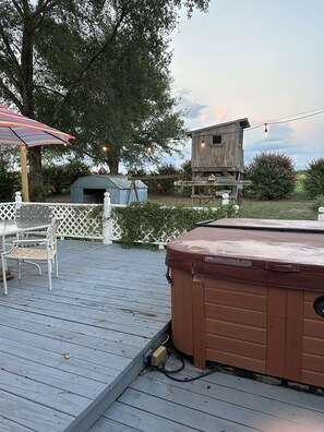 Une terrasse en bois avec un jacuzzi, une structure en bois ressemblant à une nichoir, et des guirlandes lumineuses.