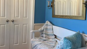 Una stanza con una panca bianca, un muro blu, una porta bianca e uno specchio con cornice dorata.