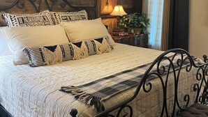 Ein Schlafzimmer mit Bett, Deckenventilator, Nachttisch mit Lampe und Fenster mit Vorhängen.