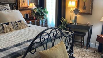 A well-appointed bedroom with a large bed, a bedside table with a lamp, a small desk with a mirror, and a potted plant.