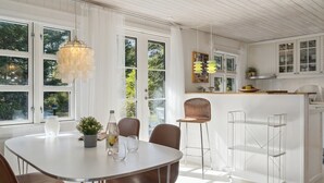 Une cuisine lumineuse avec des meubles blancs, un coin repas doté d’une table ronde et de chaises, et un bar avec des tabourets.