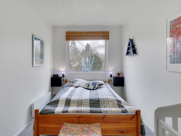 A bedroom with a wooden bed, a window with a view of trees, bedside tables with lamps, and a wall-mounted shelf.