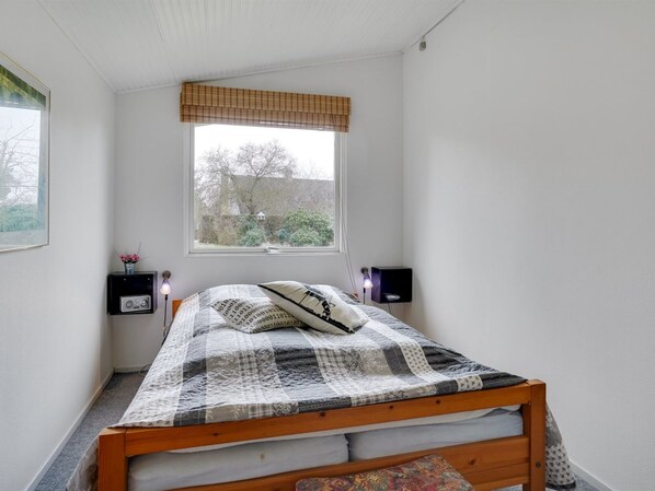 Un dormitorio con cama, ventana, mesita de noche y lámpara.