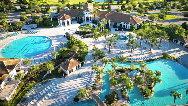 Un resort con un amplio espacio de piscina, numerosas tumbonas y un campo de golf al fondo.
