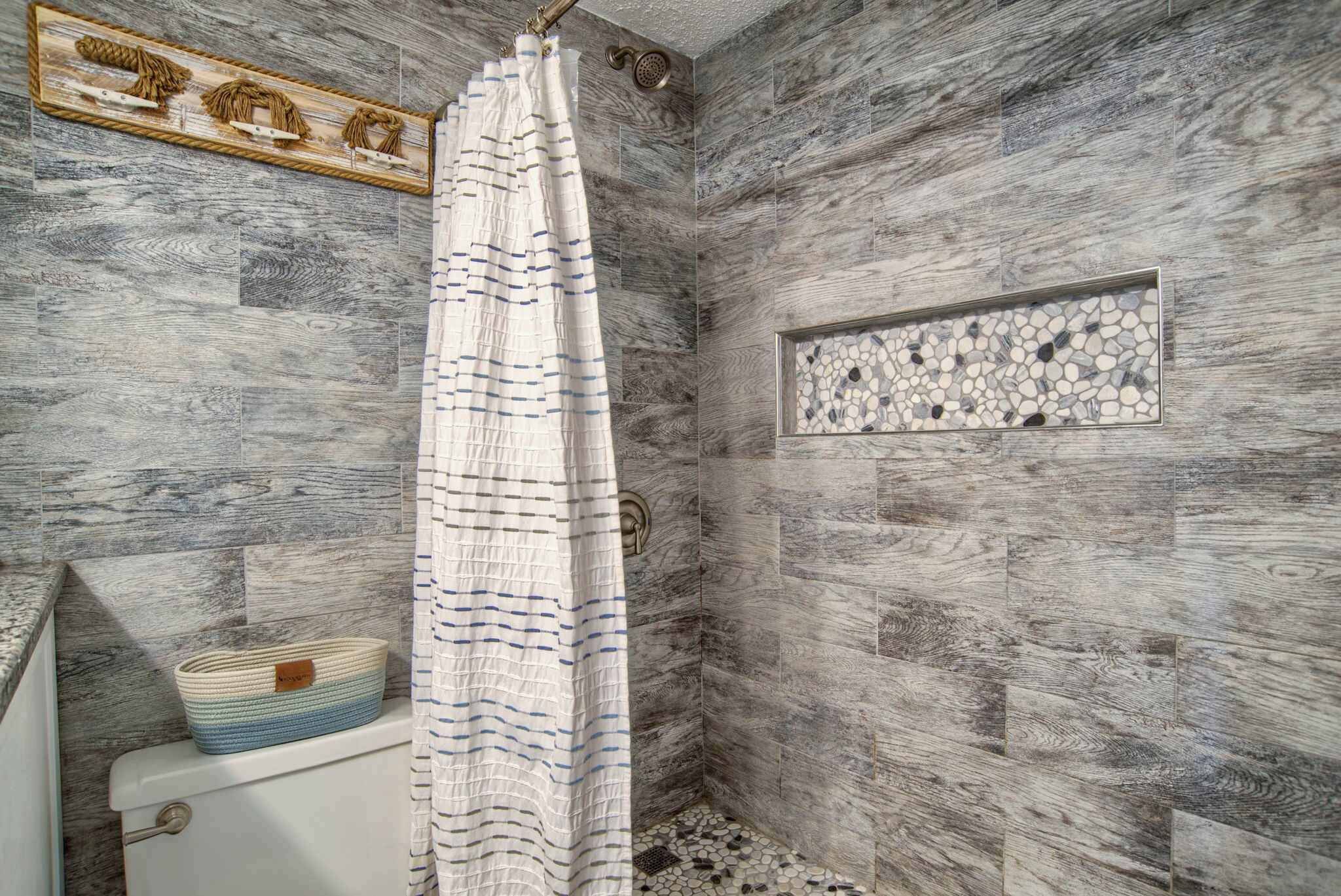 A shower with a wooden wall and a mosaic tile accent.