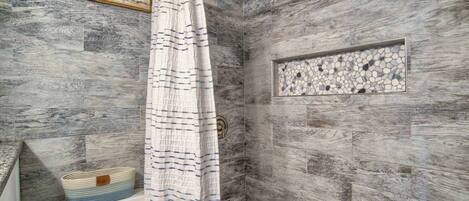 A shower with a wooden wall and a mosaic tile accent.