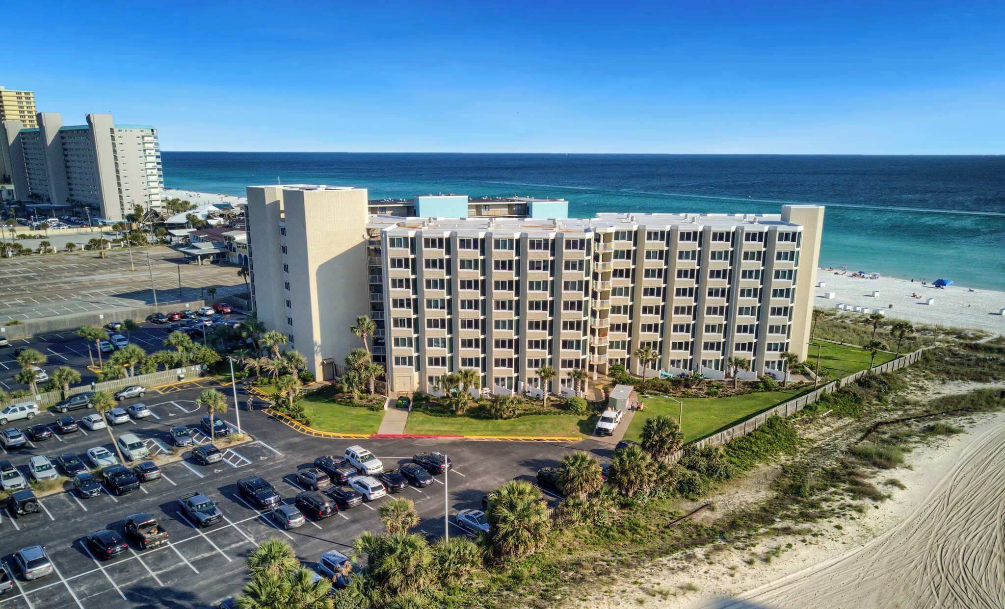 A multi-story hotel with a parking lot and a beach view.