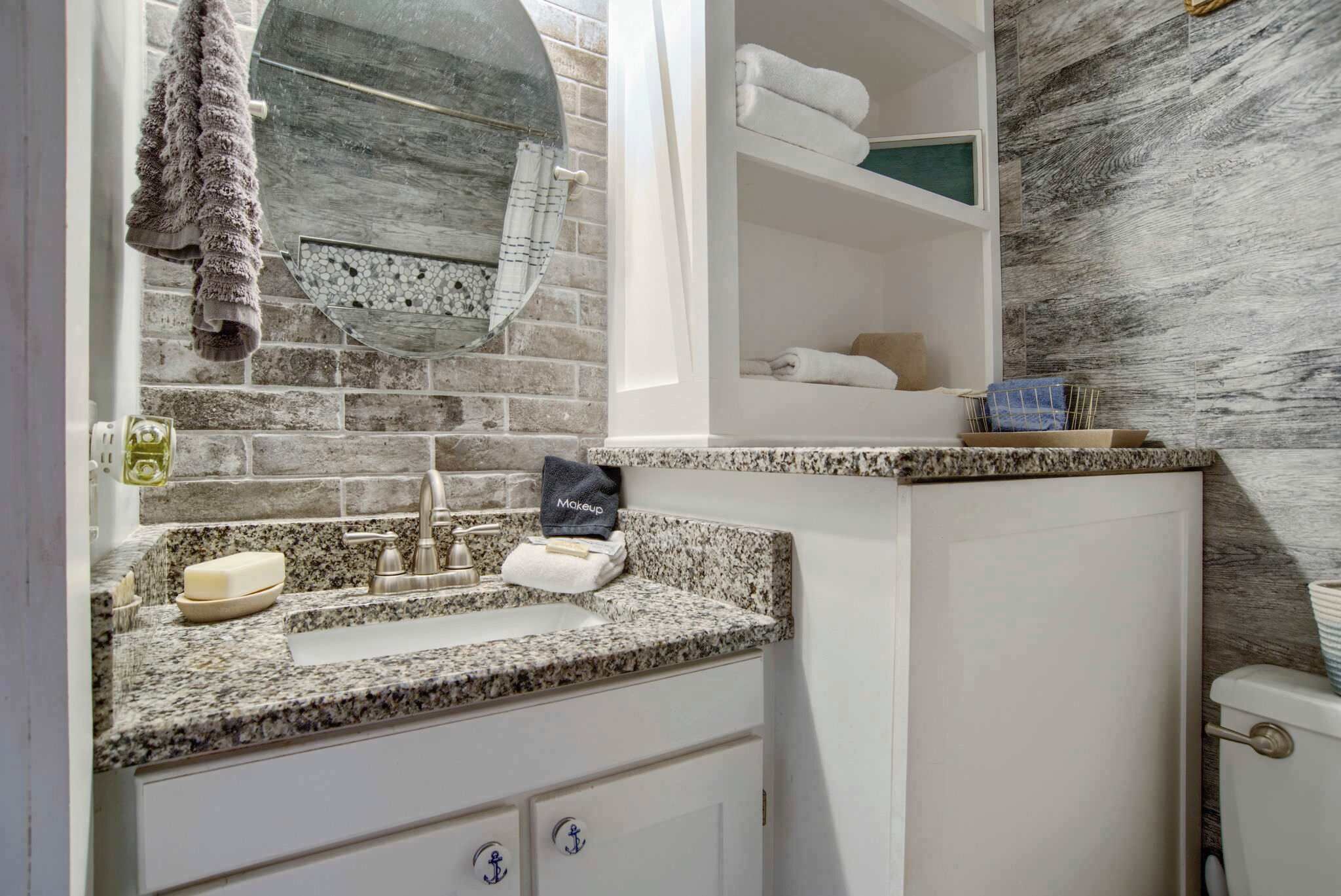 Un baño con encimera de granito, un lavabo, un perchero y un estante con toallas.