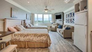 A hotel room with a large bed, a sofa, a TV, and a refrigerator.