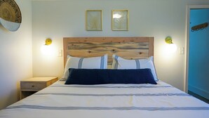 Ein Bett mit gestreifter Bettdecke, zwei Kissen, einem Holz-Kopfteil, Nachttischlampen und gerahmten Bildern an der Wand.