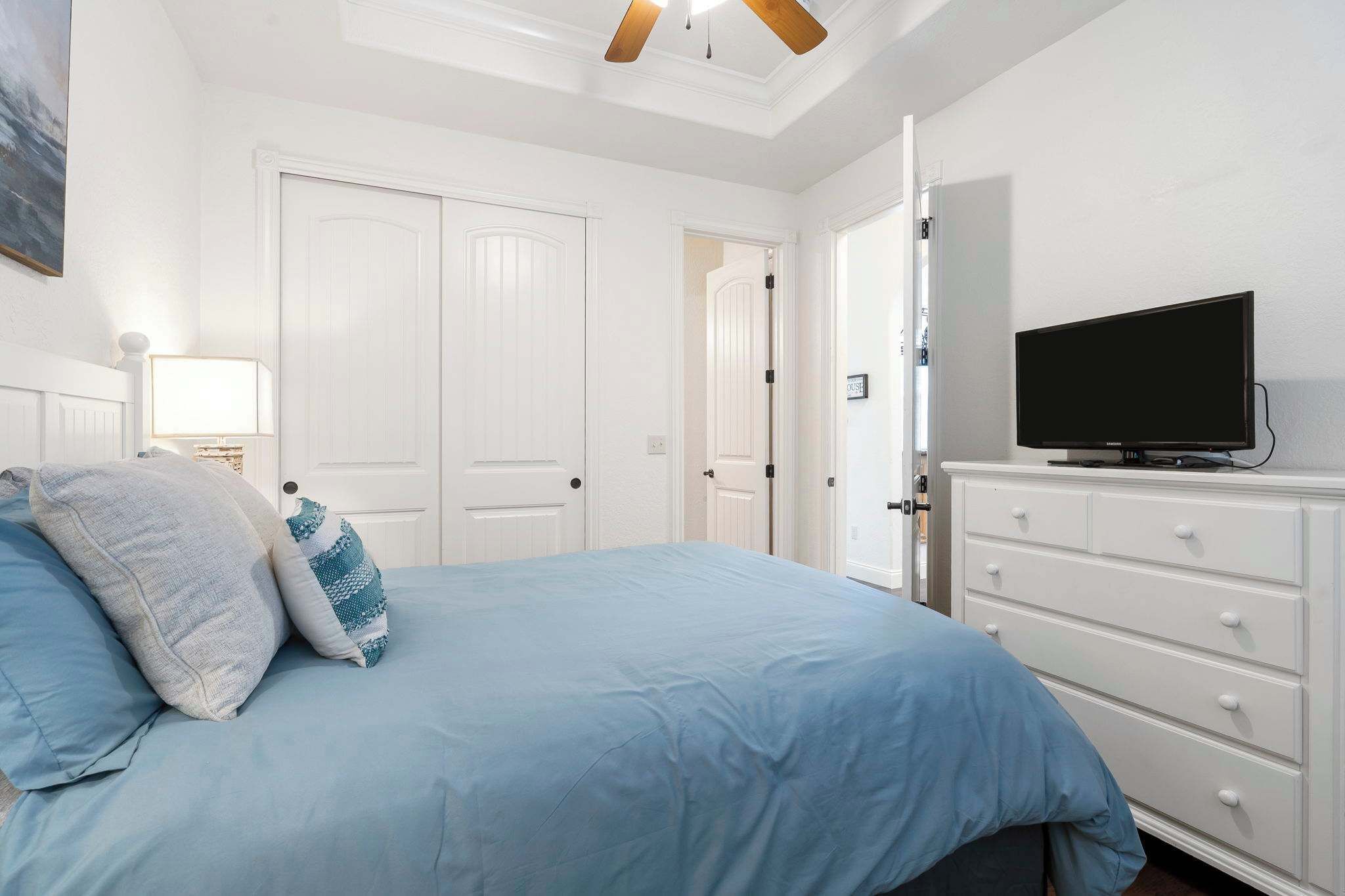 Une chambre à coucher avec un lit, un téléviseur posé sur une commode et des portes blanches.