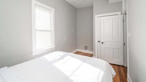 A bedroom with a bed, a ceiling fan, a window with blinds, and a door. - Suites on Main 3 (Covington)