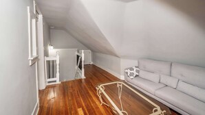 A small, open-plan living space with a wooden floor, a grey sofa, and a white radiator. - Suites on Main 3 (Covington)