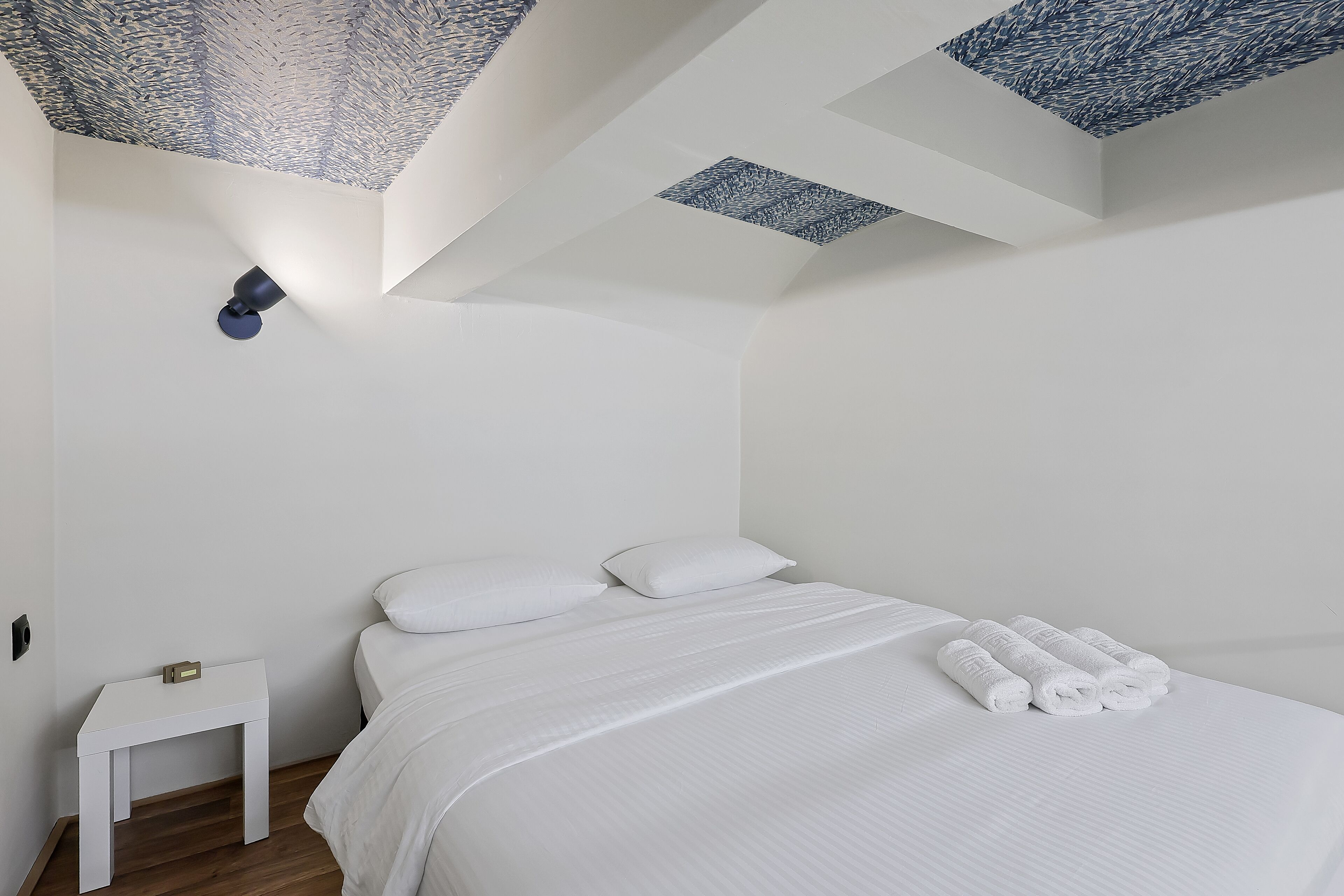 A bedroom with a bed, pillows, a nightstand, and a ceiling with a geometric pattern.