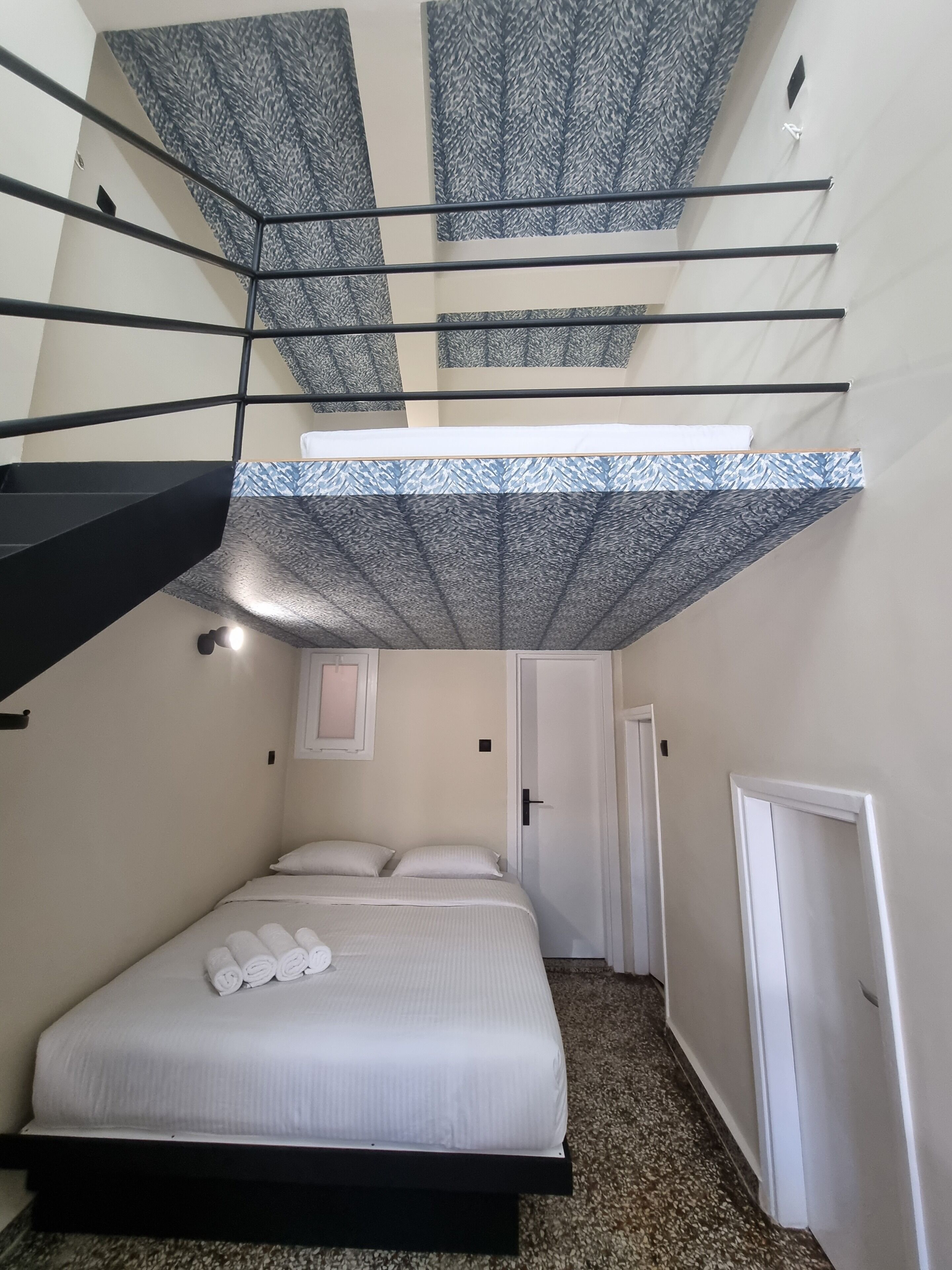 A compact bedroom with a bed, a small window, and a staircase leading to an upper level.