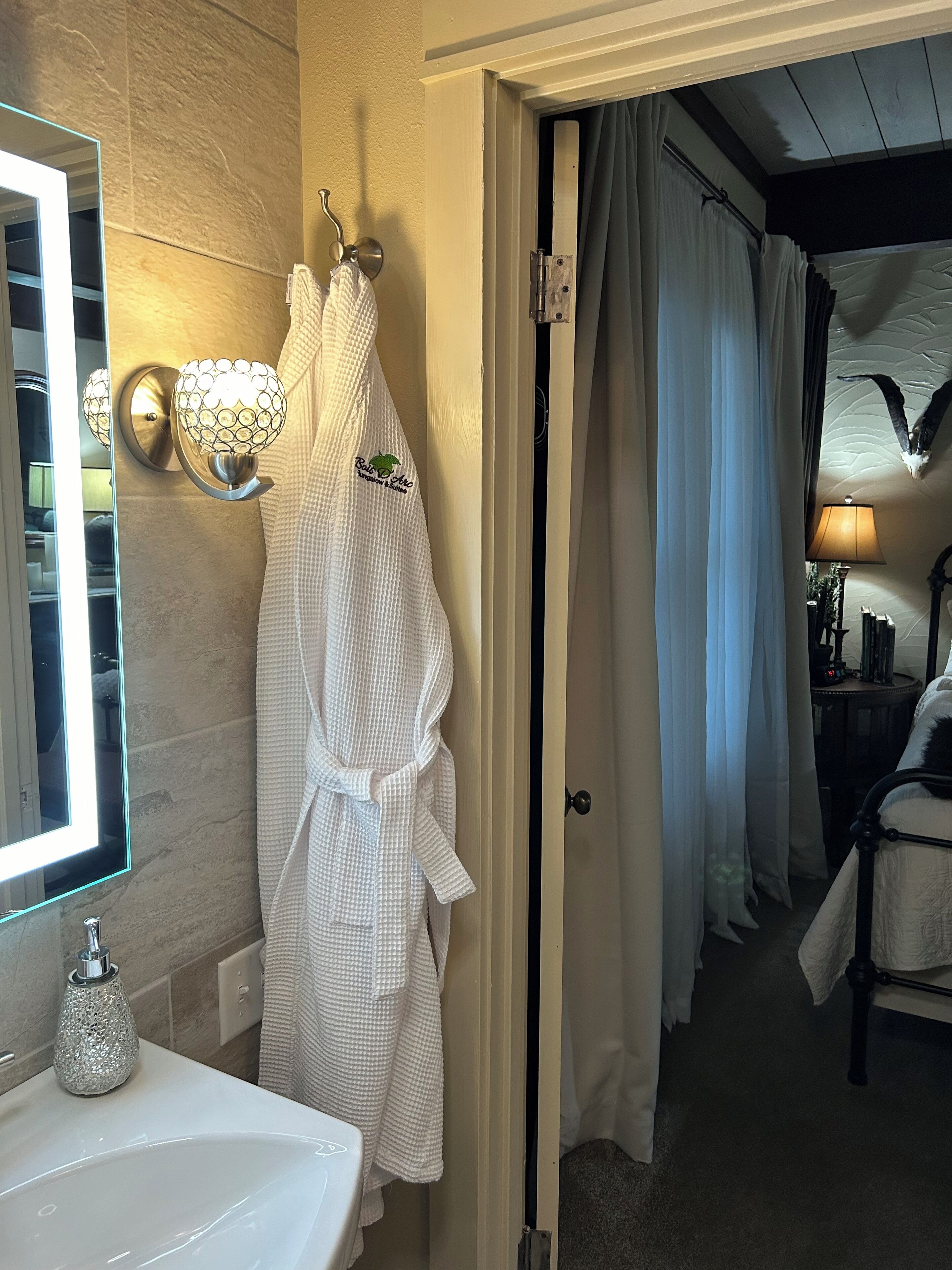 A bathroom with a white sink, a mirror, and a robe hanging on a hook.