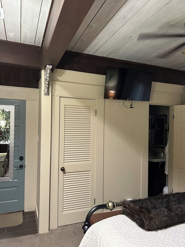 A bedroom with a bed, a door, a closet, and a television mounted on the wall.