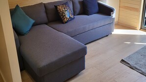 Een moderne woonkamer met een grijze modulaire bank, een blauwgroene sierkussen en een decoratief kussen met een pauwendessin.