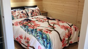 Een slaapkamer met een houten schuine plafond, een bed met bloemenbeddelsels, en een nachtkastje met een lamp.