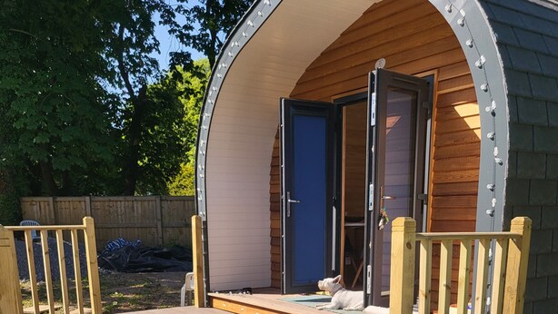 Een hottub met een houten terras en een klein houten gebouwtje met een deur op de achtergrond.