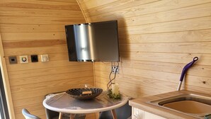 Een kleine keuken met een ronde tafel, stoelen, een spoelbak en een televisie die aan de muur is bevestigd.