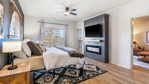 A modern bedroom with a bed, a TV, a fireplace, and a ceiling fan. - T Time Getaway - Overlooking Golf Views! (Branson West)
