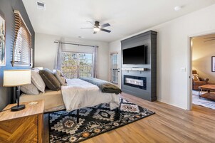 A modern bedroom with a bed, a TV, a fireplace, and a ceiling fan.
