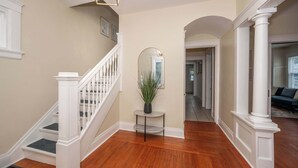 Un couloir doté d’un plancher en bois, de colonnes blanches, d’un escalier avec des rampes blanches et d’une plante en pot posée sur une petite table.