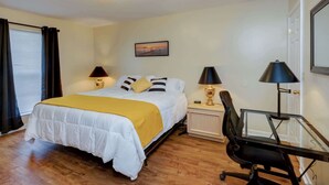 Habitación de hotel con cama, dos mesitas de noche con lámparas, un escritorio con silla y un cuadro en la pared.