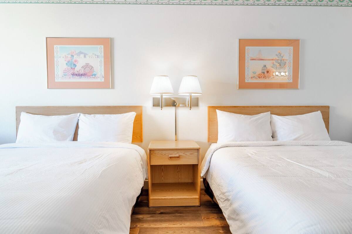 Hotellihuone, jossa on kaksi sänkyä, yöpöytä valaisimineen ja kaksi kehystettyä kuvaa seinällä.