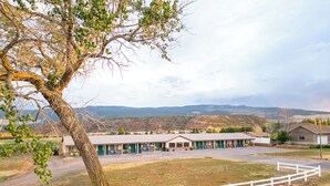 Un motel con varias habitaciones, un estacionamiento cercado y vistas a montañas distantes.