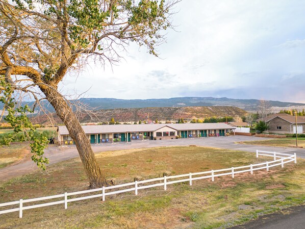 Un motel con varias habitaciones, un estacionamiento cercado y vistas a montañas distantes.