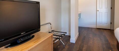 Ein Zimmer mit einem Flachbildfernseher auf einem hölzernen Standfuß, einem Metall-TV-Möbel, einer weißen Tür und einem Flur mit Holzboden.