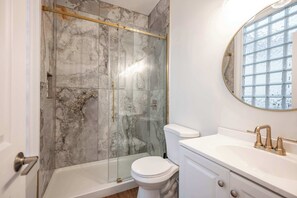 Une salle de bain avec une douche à parois de verre, des toilettes blanches et un meuble-lavabo avec un robinet doré.