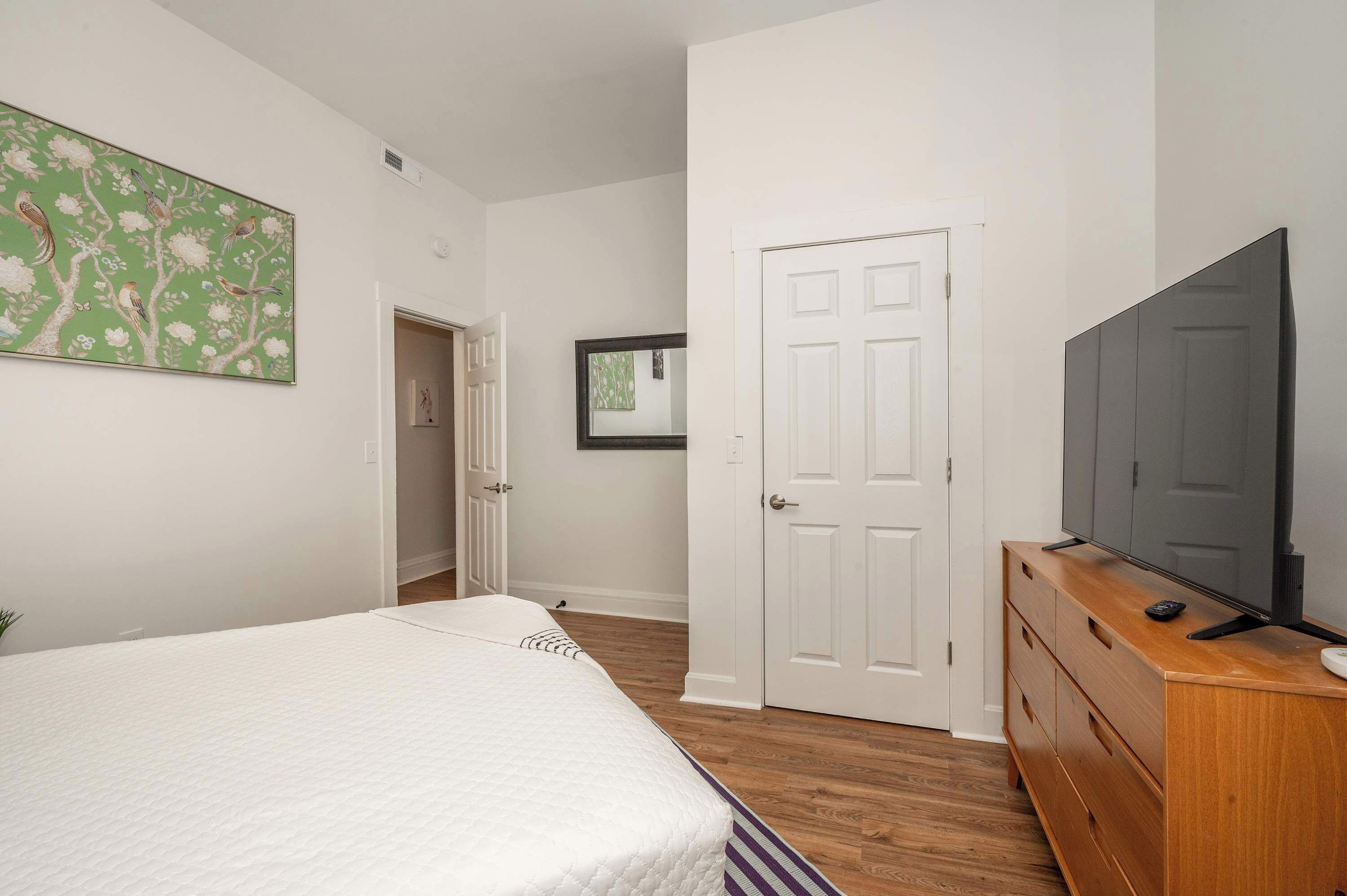 Un dormitorio con cama, cómoda, televisor y puerta.