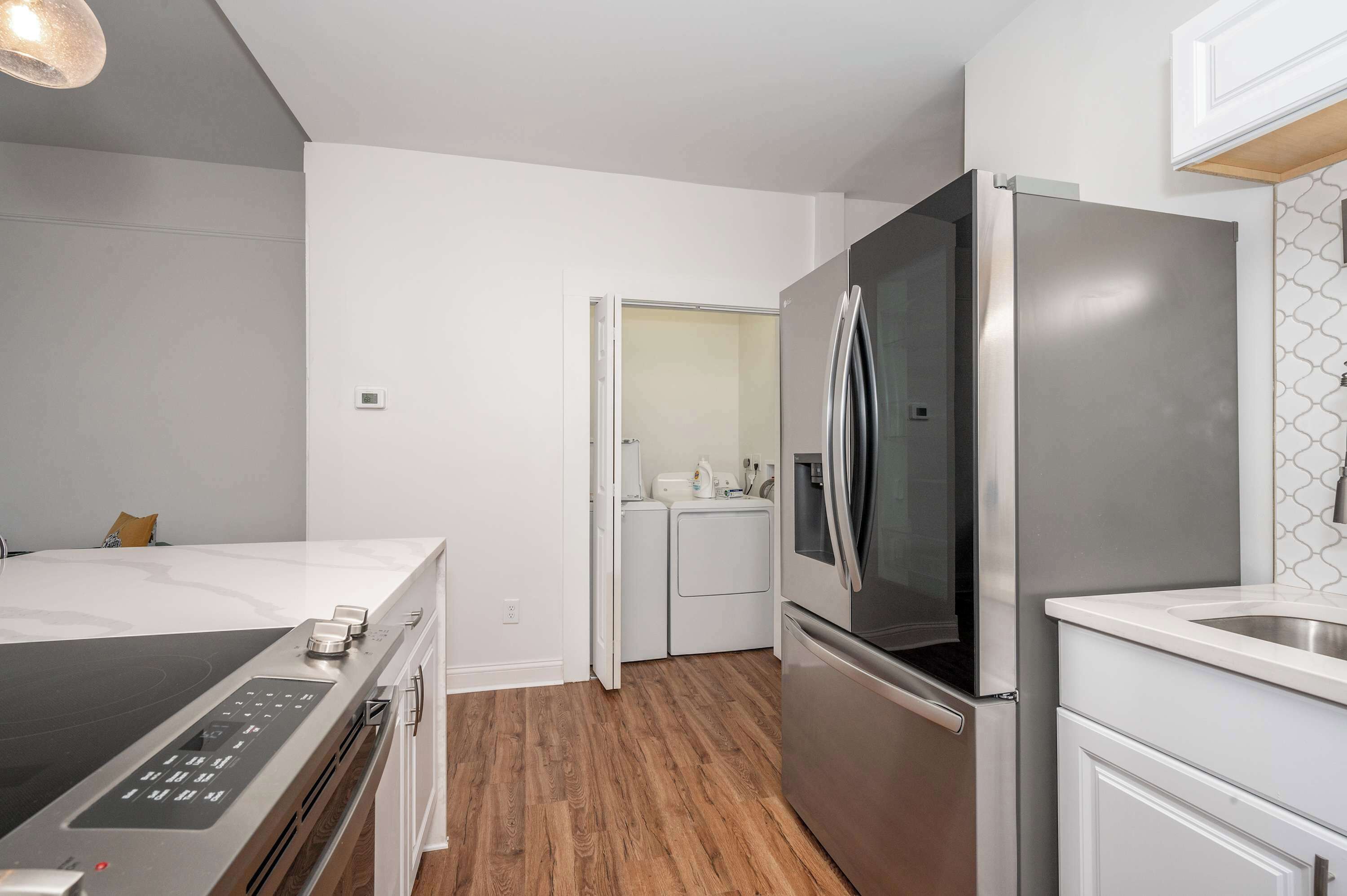 A modern kitchen with a built-in oven, a stainless steel refrigerator, and a wooden floor.