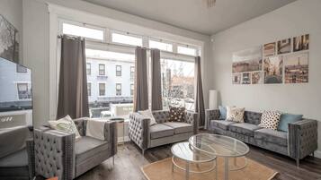 A modern living room with a grey sofa set, a glass coffee table, and a large window with curtains.