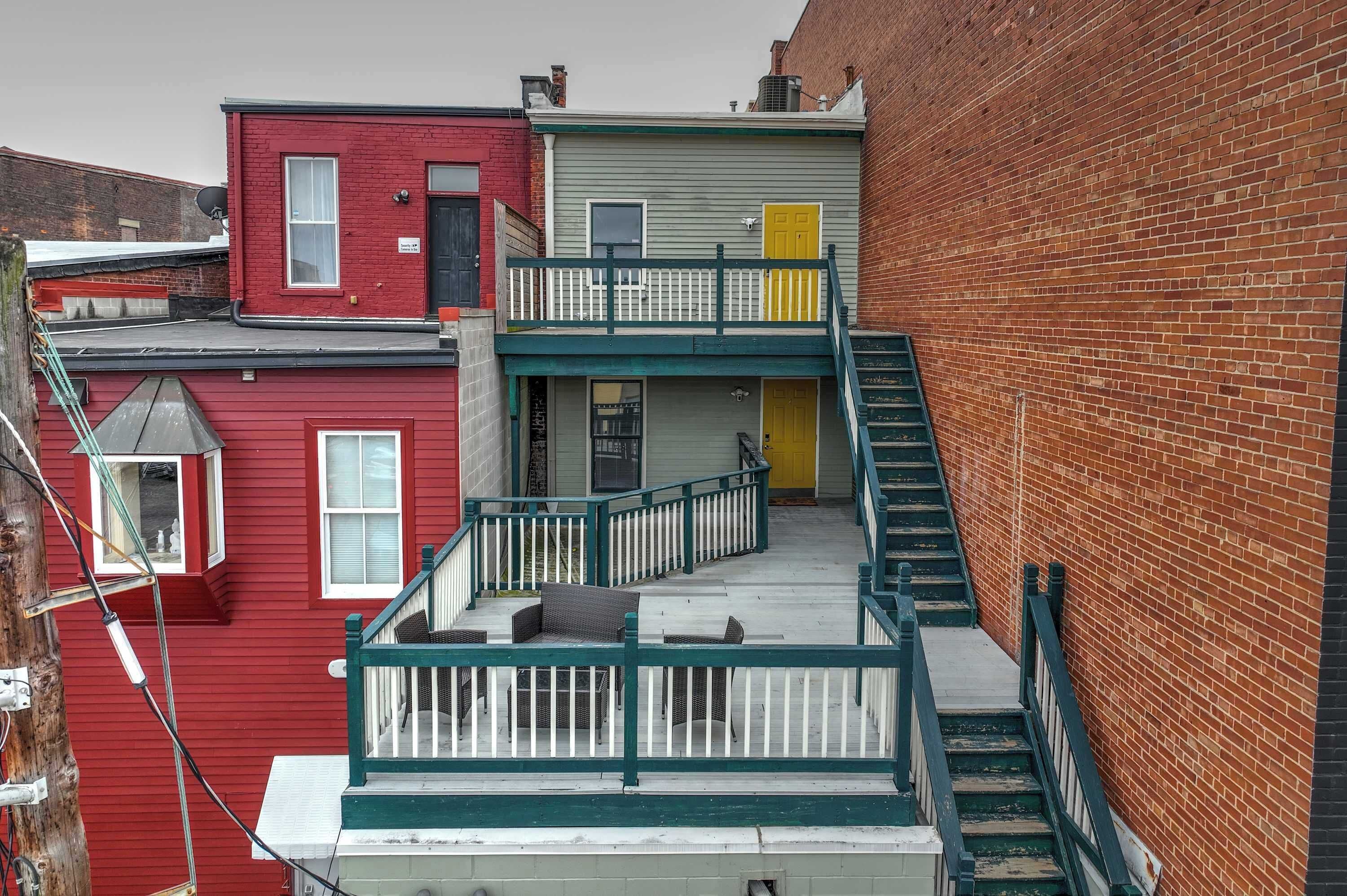 Un immeuble à plusieurs étages dont la façade est rouge, grise et jaune. Il est doté d’un balcon avec des balustrades blanches et d’un escalier menant aux étages supérieurs.