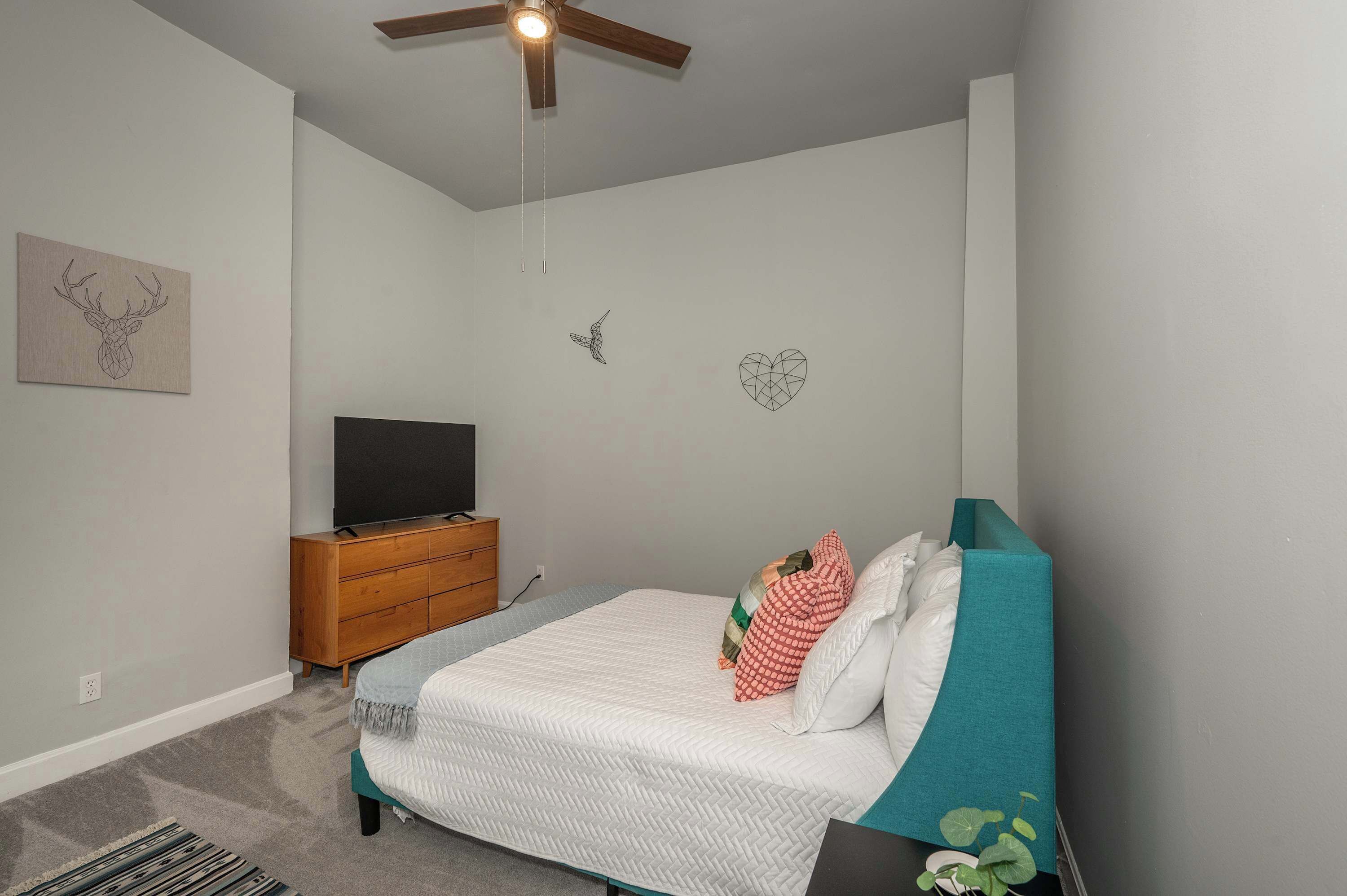 A bedroom with a bed, a wooden dresser, a television, and wall art.