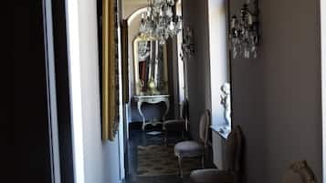 A hallway with ornate chandeliers, antique furniture, and a patterned rug.