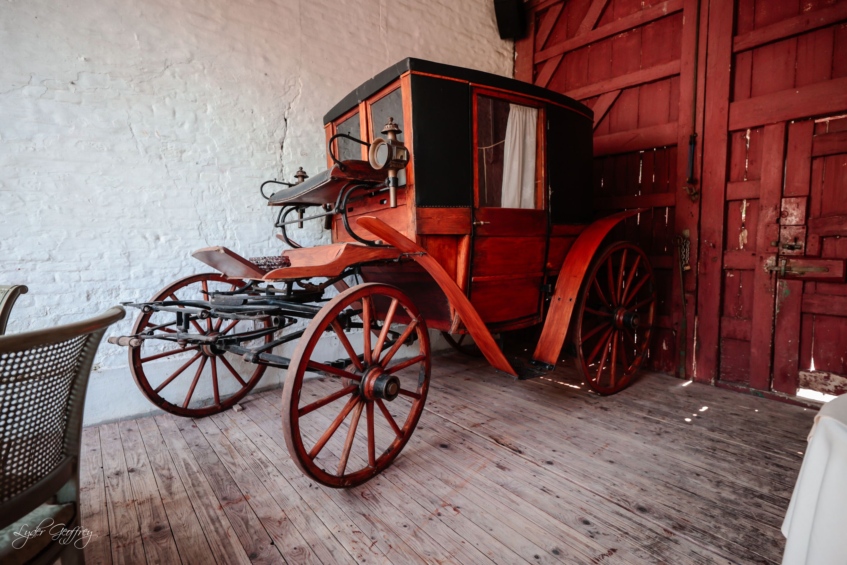 An antique carriage parked inside a building with wooden floors and red doors.