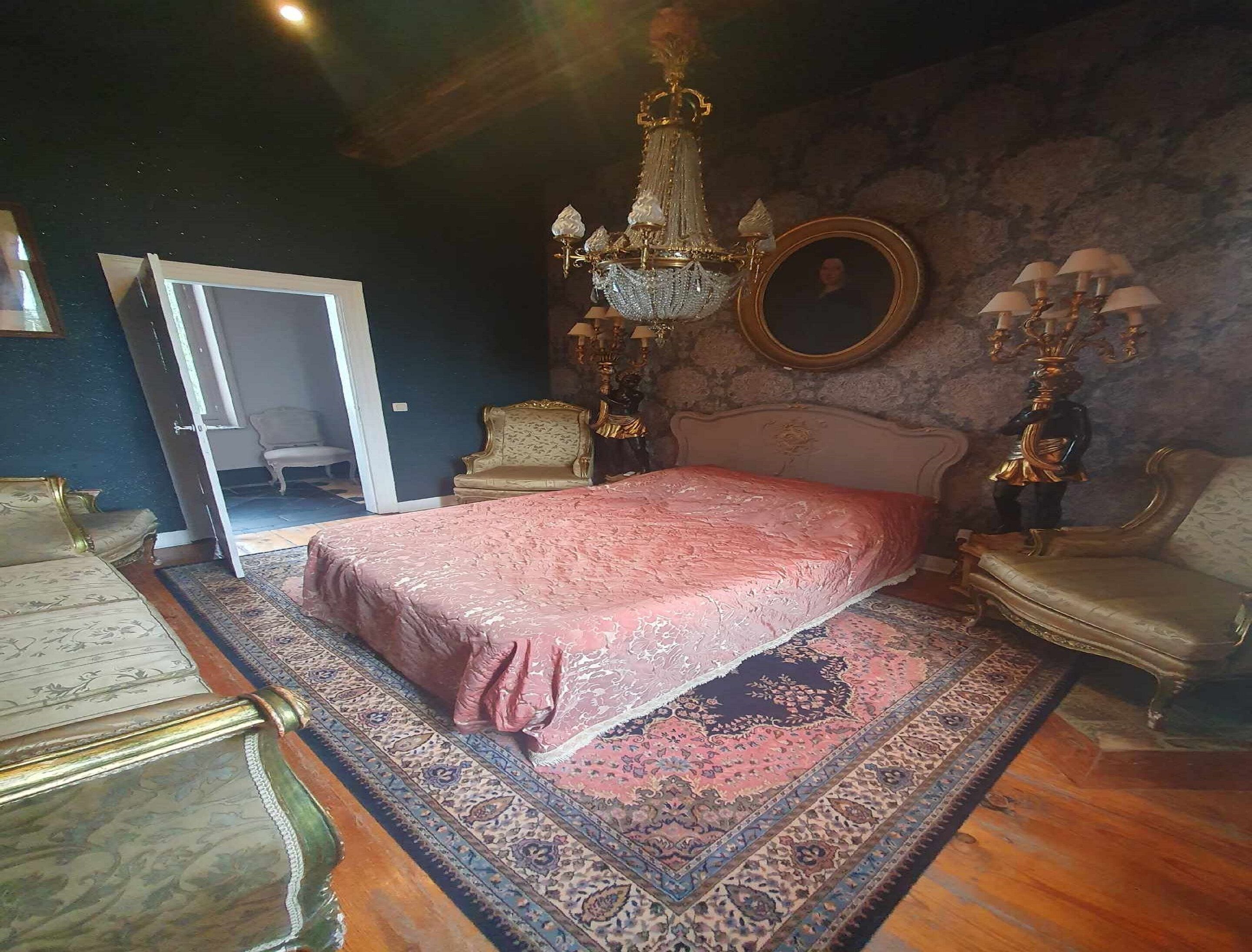 A bedroom with a large bed, ornate chandelier, and classic furniture.