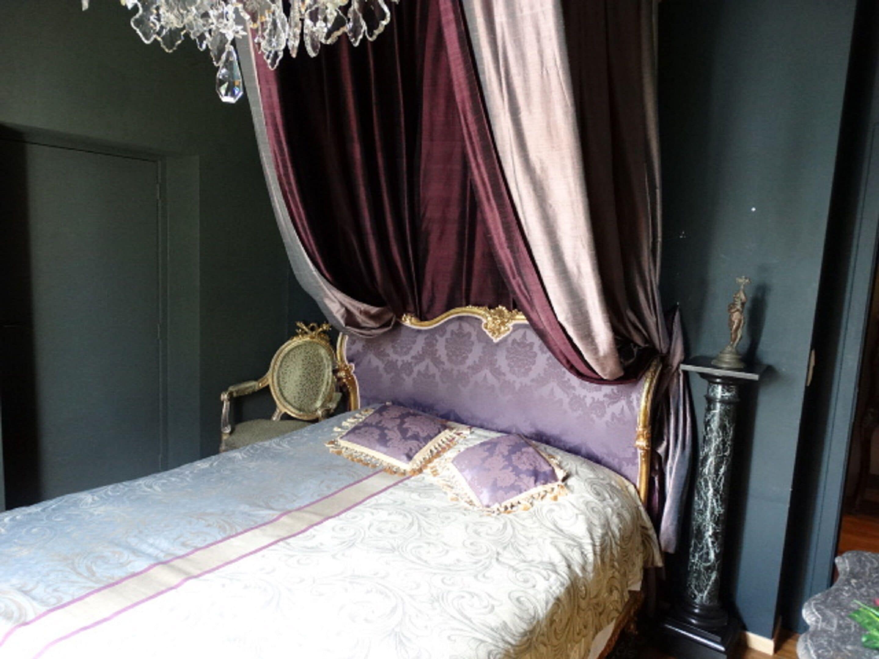 A bedroom with a canopy bed, a mirror, a statue, and a tall column.