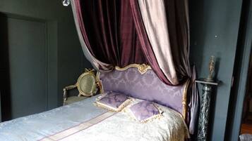 A bedroom with a canopy bed, a mirror, a statue, and a tall column.
