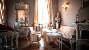 A classic interior with a round table, a sofa, a mirror, and a fireplace.