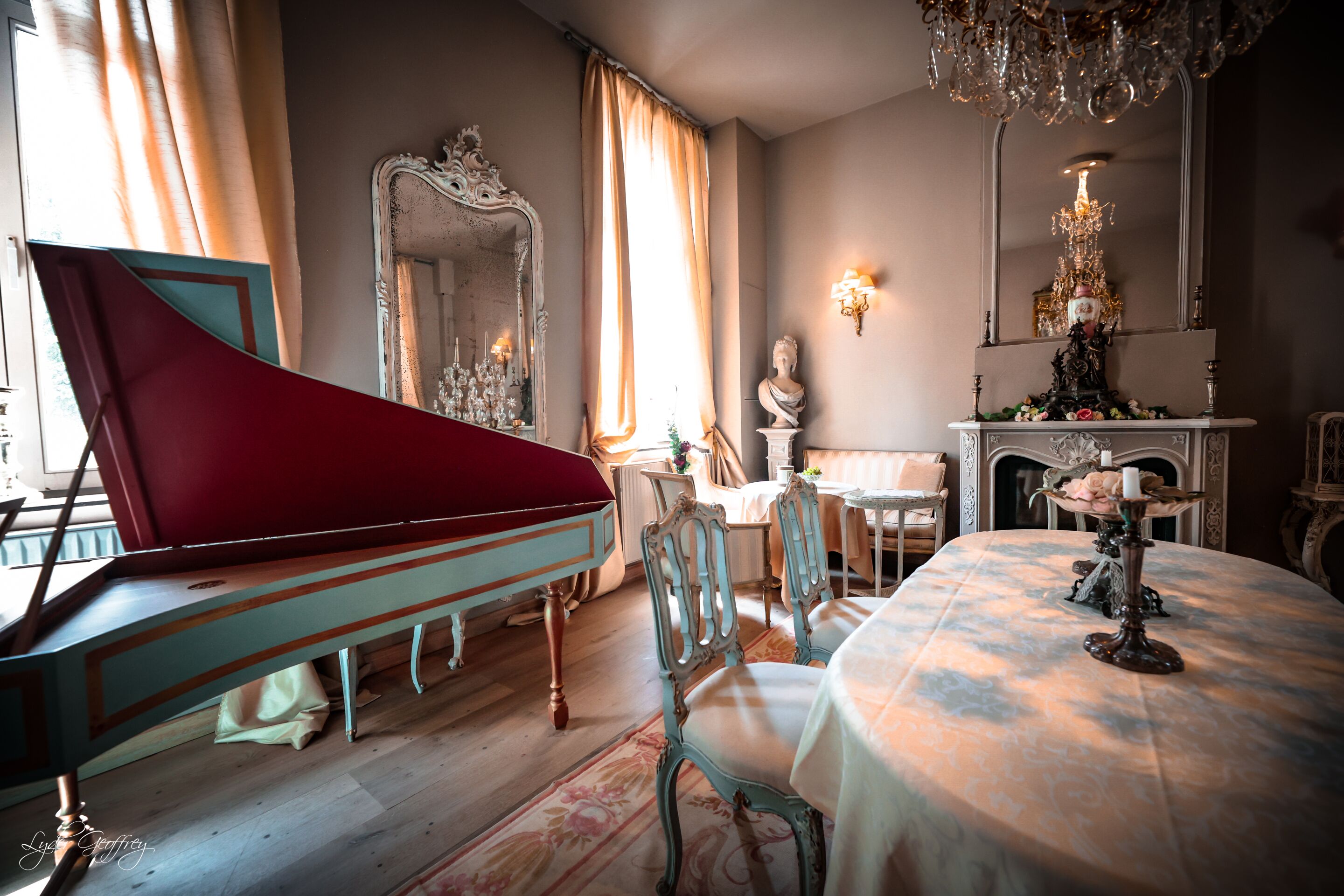 A grand room with a piano, ornate chairs, a table with a candle, and a mirror with a statue.
