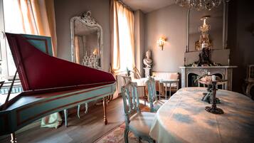 A grand room with a piano, ornate chairs, a table with a candle, and a mirror with a statue.