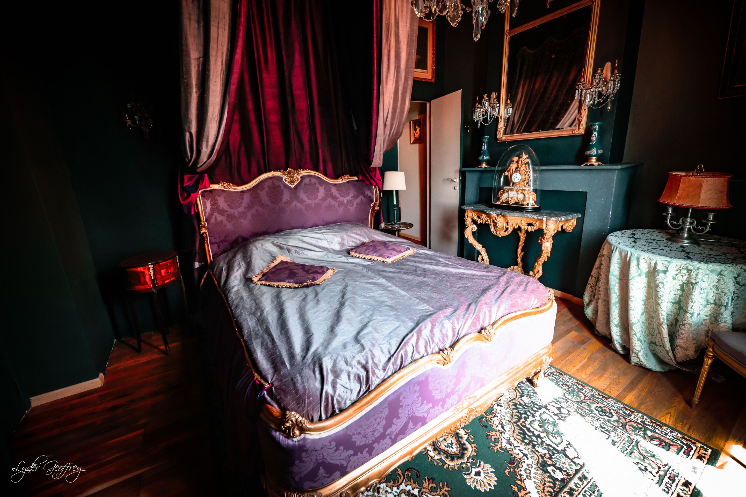 Une chambre à coucher avec un grand lit, un lustre, un miroir et une petite table avec une lampe.